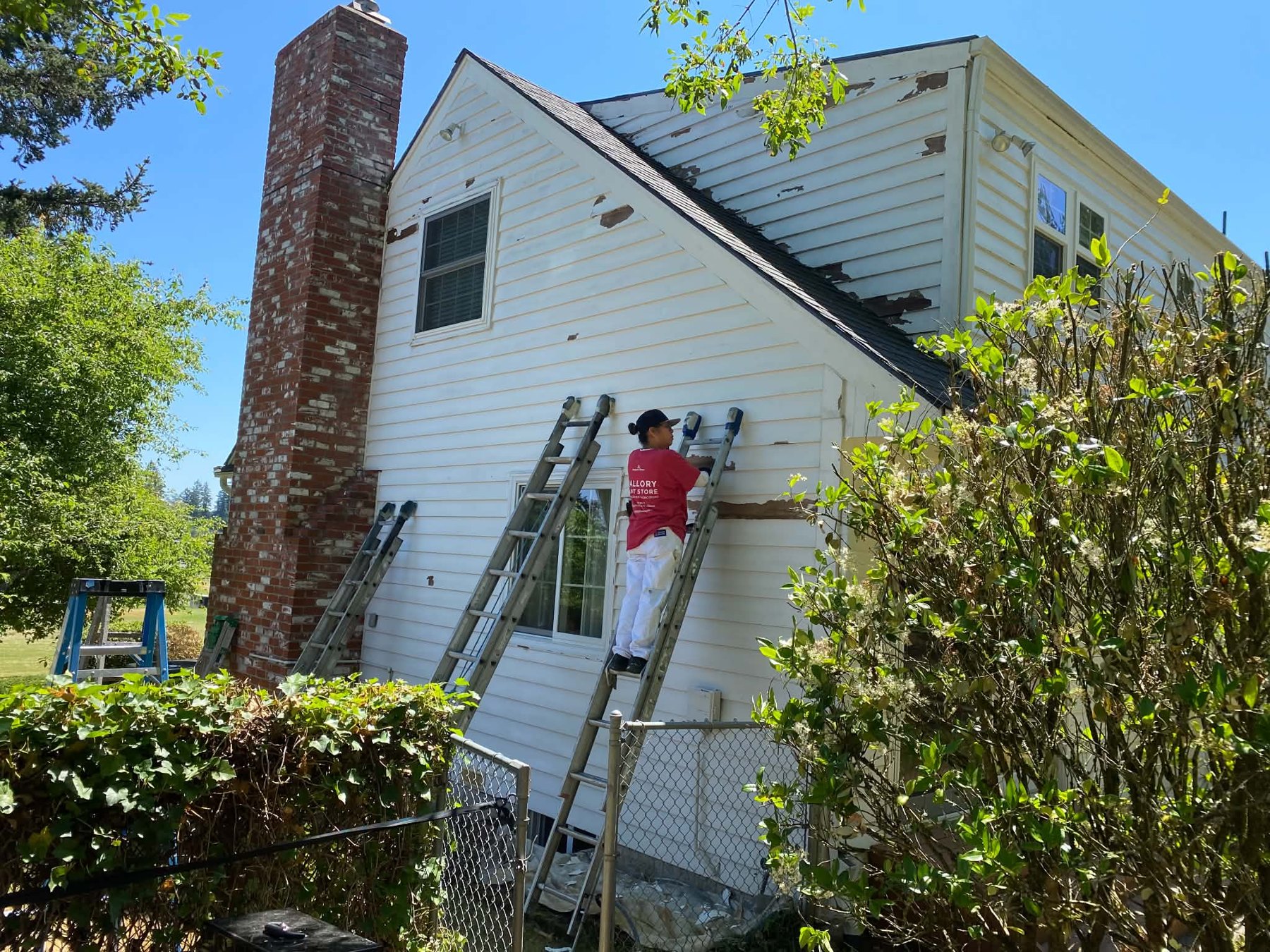 Painter working on white exterior siding beside a brick chimney